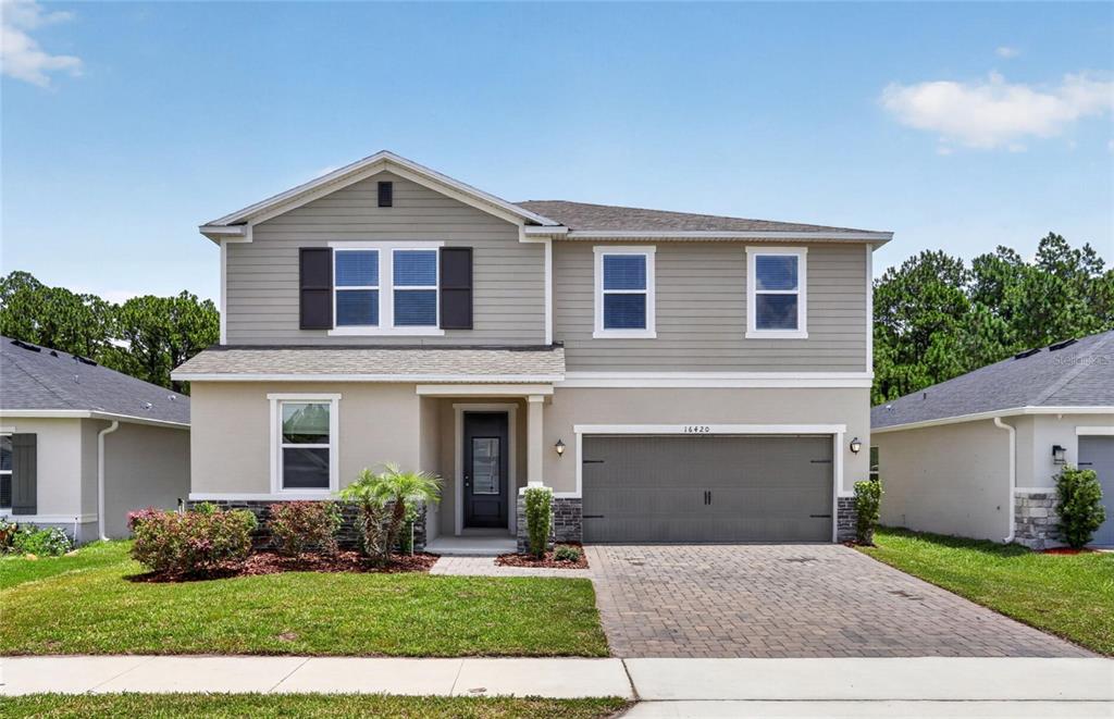 A two-story suburban house features beige stucco, grey horizontal siding, and a two-car garage — 16420 WINDING PRESERVE CIRCLE, CLERMONT, FL