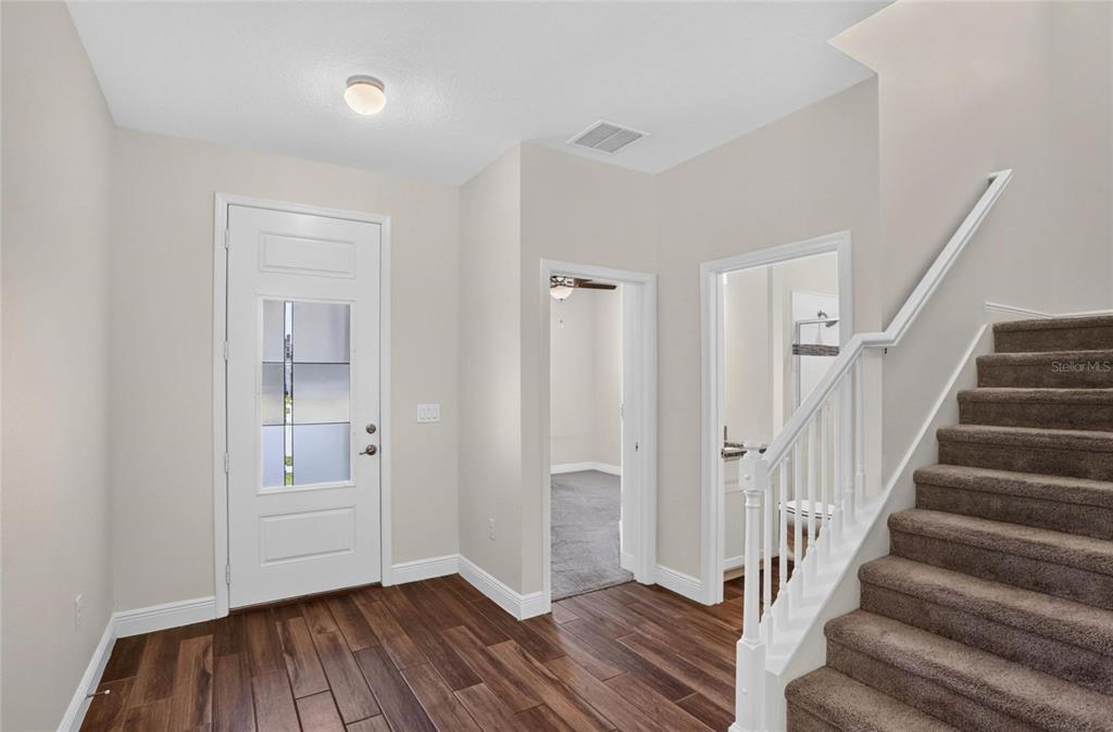 An entryway with wood-look flooring, a white front door, a staircase, and two interior doorways — 16420 WINDING PRESERVE CIRCLE, CLERMONT, FL