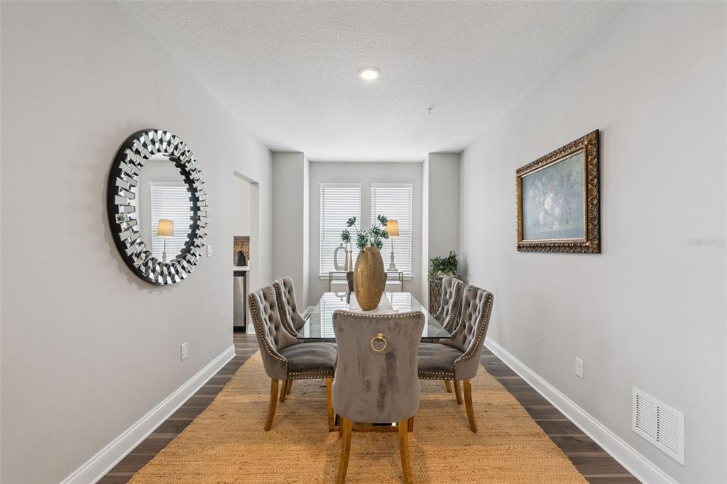 A dining room features a glass table, gray tufted chairs, a round mirror, and artwork — 7521 LAUREATE BOULEVARD UNIT 5306, ORLANDO, FL