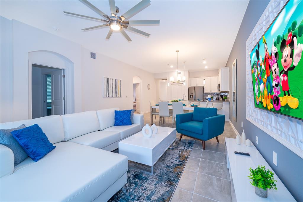 A living room features a white sectional sofa, blue accent chair, and a large television — 8899 CABOT CLIFFS DRIVE UNIT 102, DAVENPORT, FL