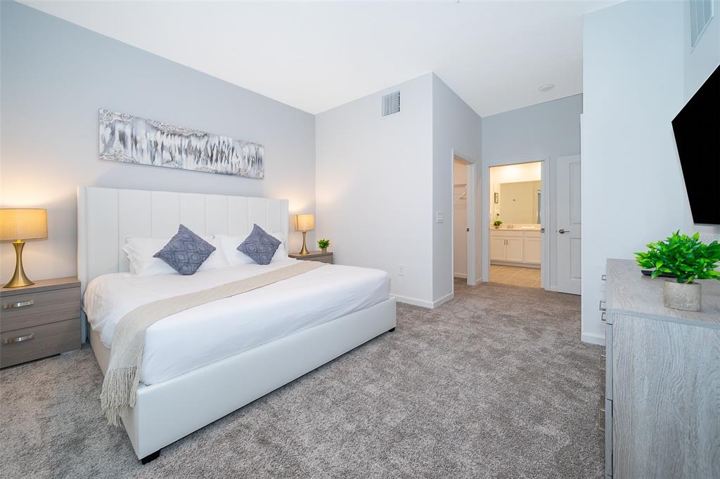 A bedroom features a white upholstered bed, gray carpet, and an attached bathroom — 8899 CABOT CLIFFS DRIVE UNIT 102, DAVENPORT, FL