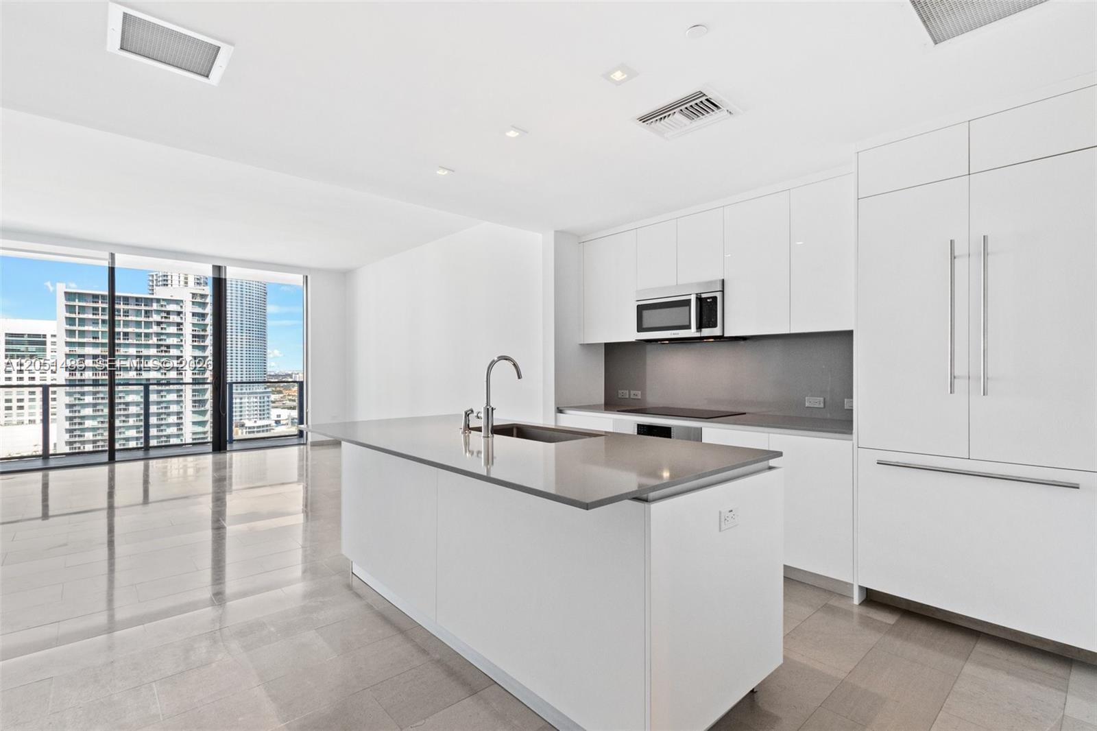 A modern kitchen features white cabinetry, a gray island countertop, and floor-to-ceiling windows — 68 SE 6th St # 1706, Miami FL 33131, MIAMI, FL