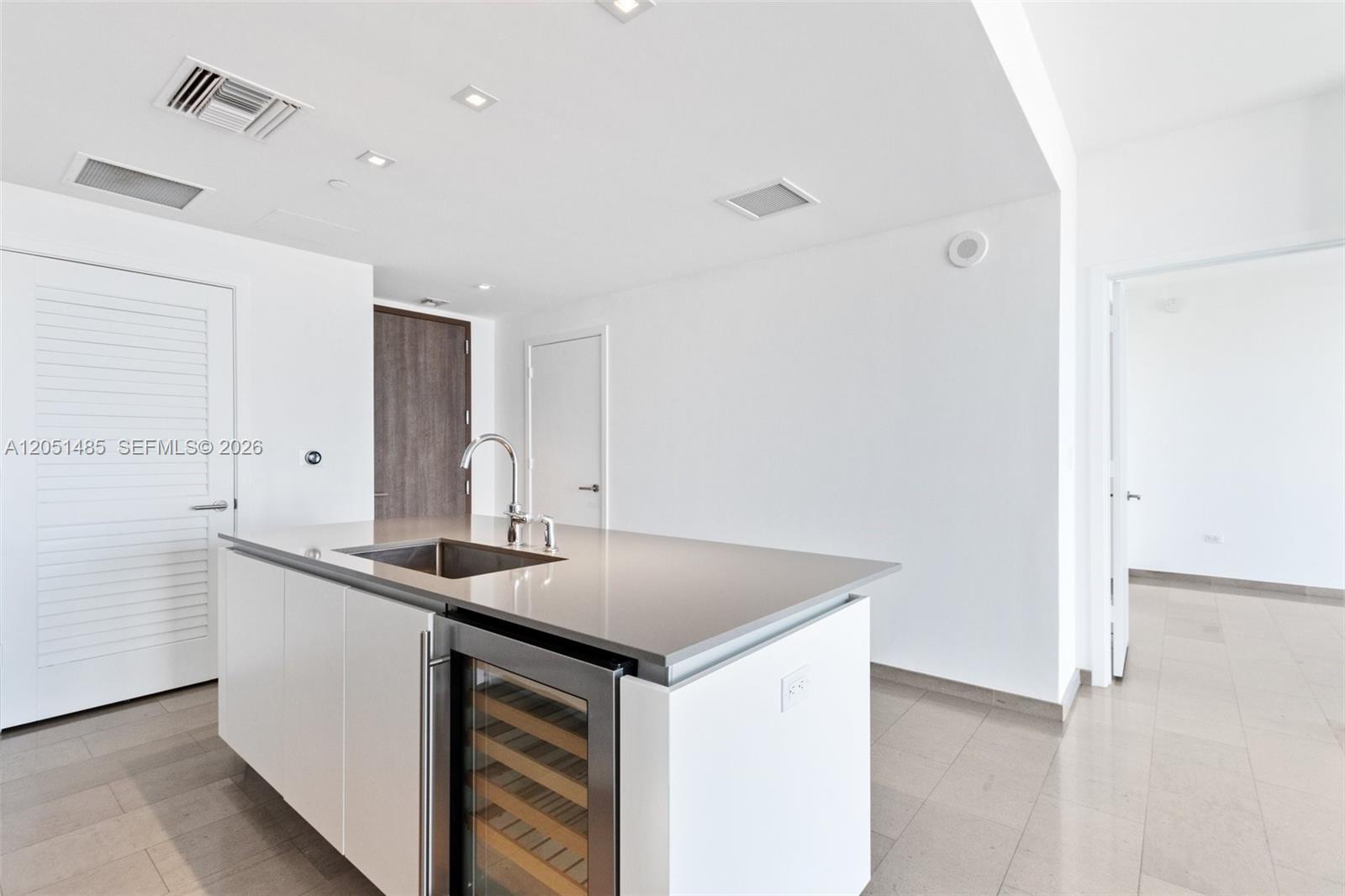 A modern kitchen island with a sink and wine cooler sits in a white room — 68 SE 6th St # 1706, Miami FL 33131, MIAMI, FL