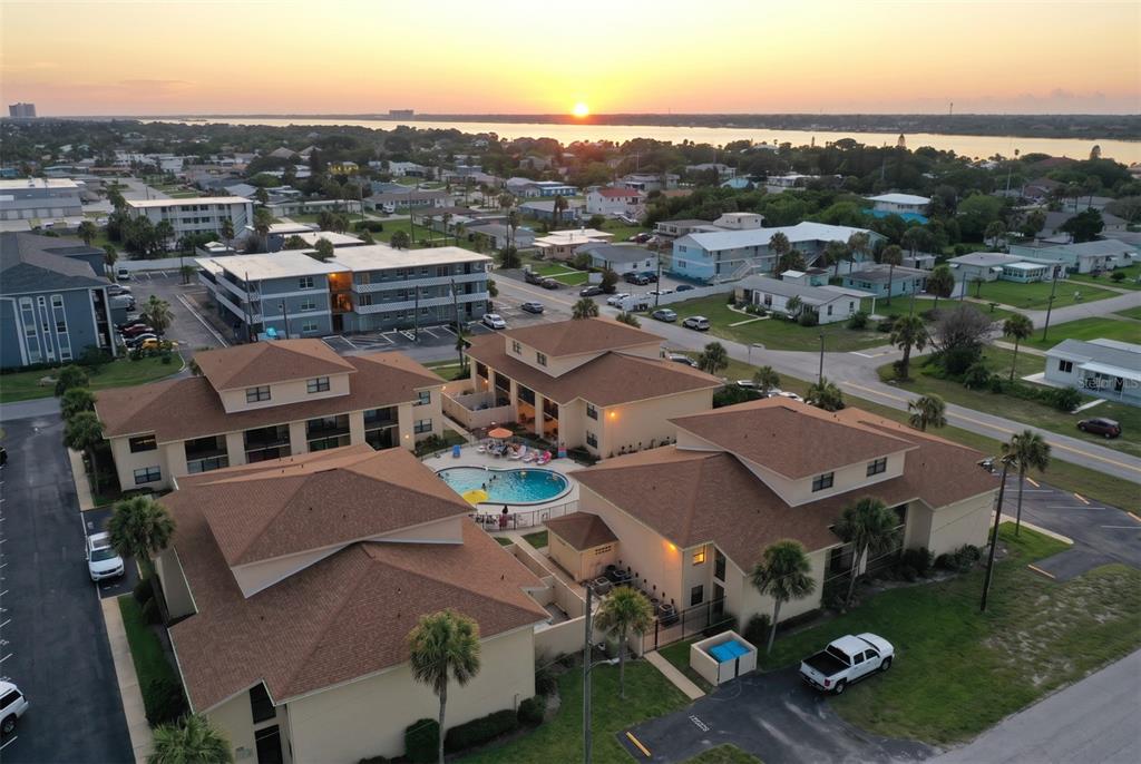 An aerial view shows a multi-story apartment complex with a central swimming pool at sunset — 100 GRANT AVENUE UNIT 24, DAYTONA BEACH SHORES, FL