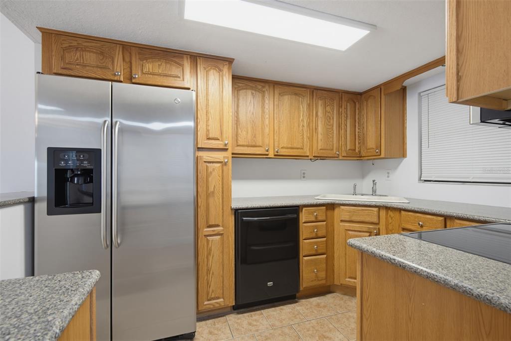 A kitchen features oak cabinets, granite countertops, a stainless steel refrigerator, and a black dishwasher — 100 GRANT AVENUE UNIT 24, DAYTONA BEACH SHORES, FL