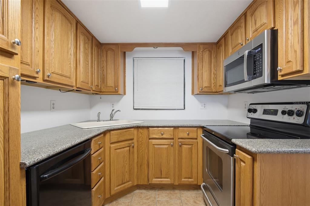 A kitchen with oak cabinets, granite countertops, stainless steel appliances, and a corner sink — 100 GRANT AVENUE UNIT 24, DAYTONA BEACH SHORES, FL