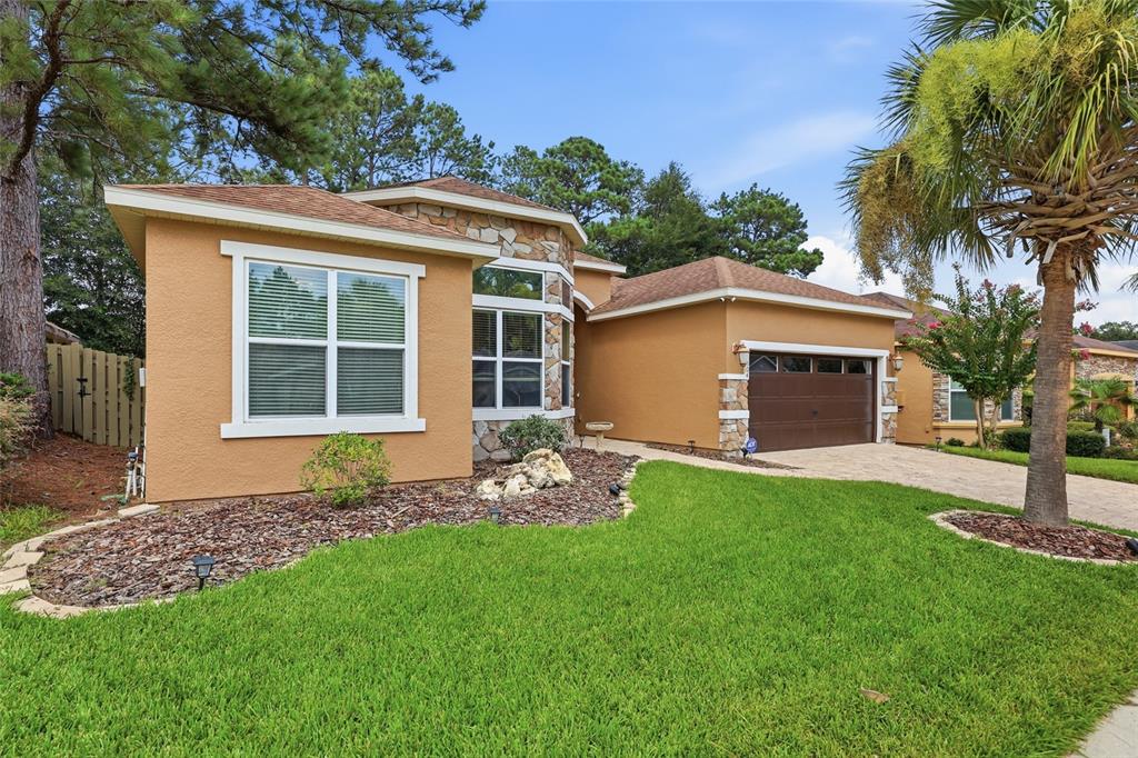 A single-story house with tan stucco, stone accents, a two-car garage, and a palm tree — 14504 NW 25TH AVENUE, NEWBERRY, FL