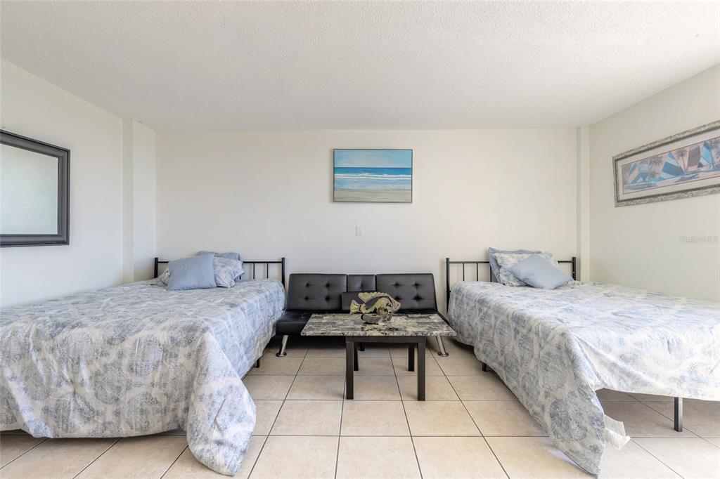 A bedroom features two twin beds, a black futon, and a coffee table on tile floors — 701 S ATLANTIC AVENUE UNIT 621, DAYTONA BEACH, FL