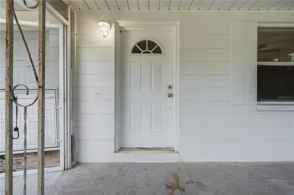 A white front door with a half-moon window is centered on a covered porch — 2122 HOLIDAY DRIVE, HOLIDAY, FL