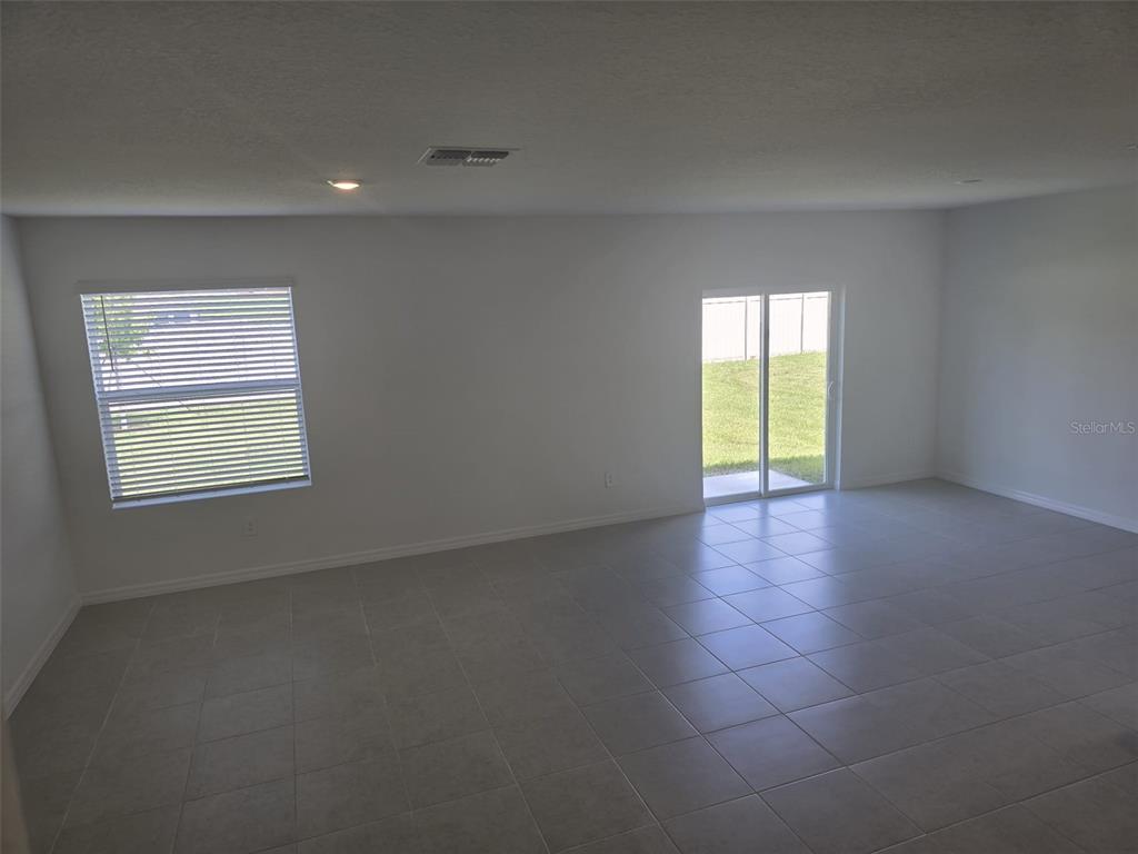 An empty room features light-colored tile flooring, white walls, a window with blinds, and sliding doors — 11962 BRAE WAY, DADE CITY, FL