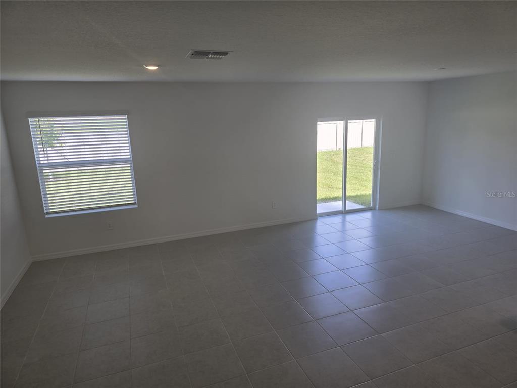 An empty room with light-colored tile flooring, a single window, and sliding glass doors — 11962 BRAE WAY, DADE CITY, FL