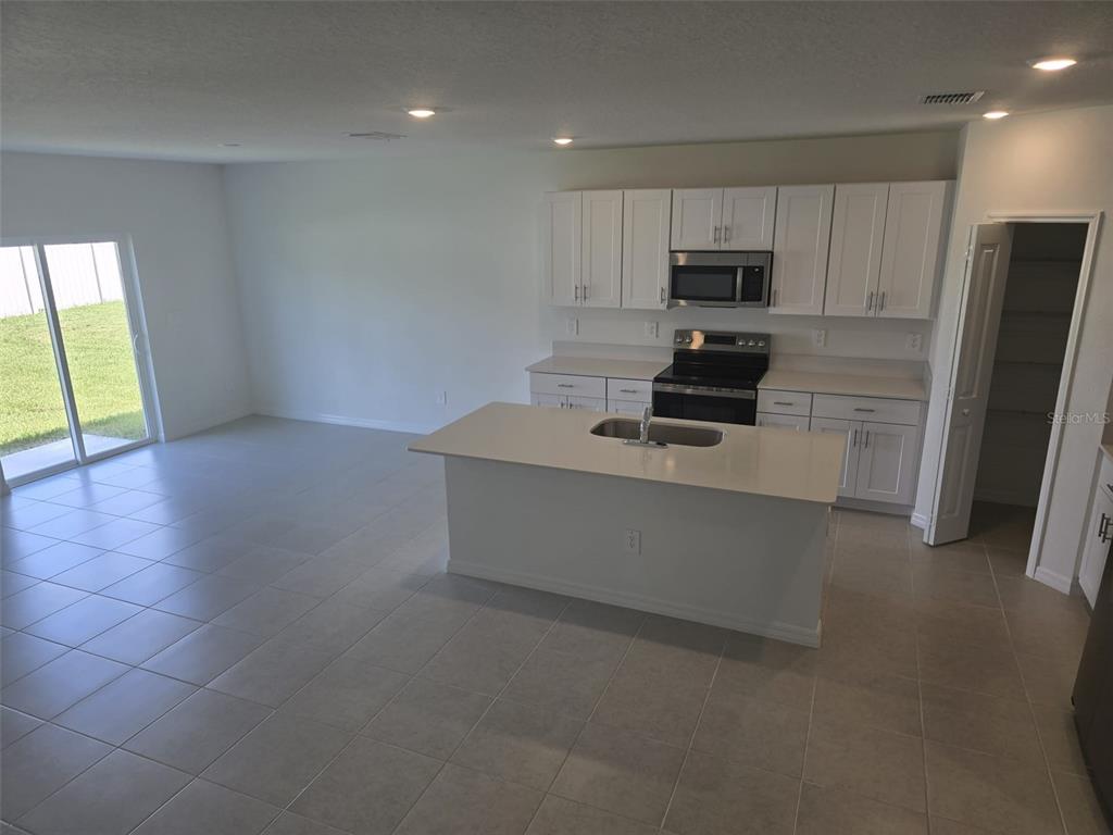 A kitchen with white cabinets, a central island with a sink, and tile flooring — 11962 BRAE WAY, DADE CITY, FL