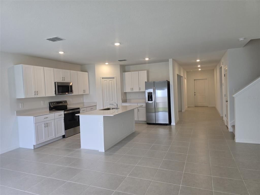 A modern kitchen features white cabinets, stainless steel appliances, a center island, and tile flooring — 11962 BRAE WAY, DADE CITY, FL