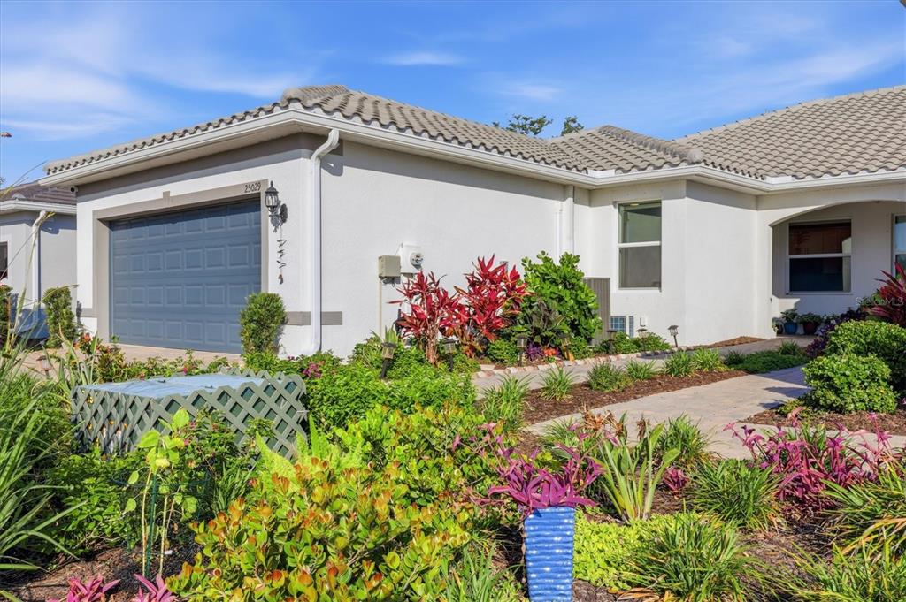 A single-story house exterior features a gray garage door, stucco walls, and a landscaped yard — 25029 PEARL LAKE CIRCLE UNIT 25029, ENGLEWOOD, FL