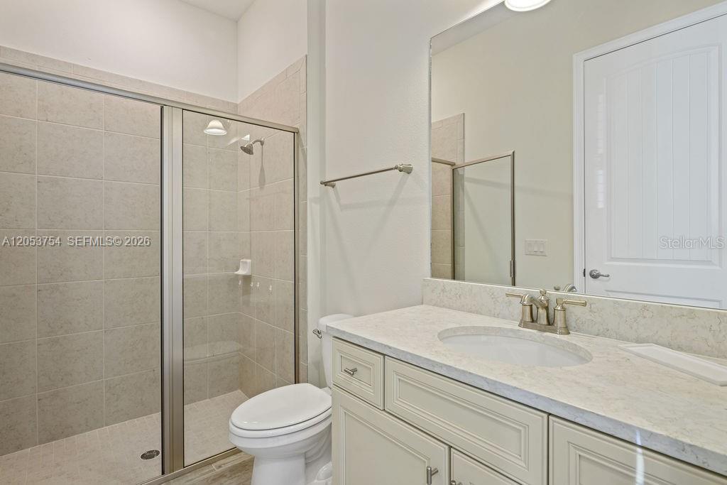 A bathroom features a walk-in shower with tiled walls, a vanity with a stone countertop, and a toilet — 8117 Surf St, Kissimmee FL 34747, KISSIMMEE, FL