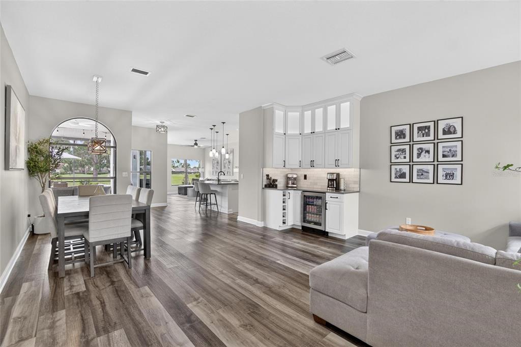 An open-concept living and dining area with wood-look flooring, white cabinetry, and a beverage cooler — 11203 LONGBROOKE DRIVE, RIVERVIEW, FL