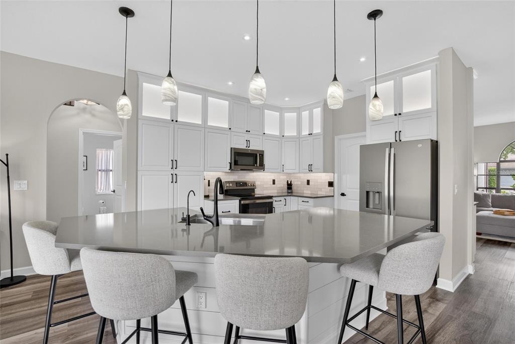 A modern kitchen features a large gray island, white cabinetry, and four gray bar stools — 11203 LONGBROOKE DRIVE, RIVERVIEW, FL