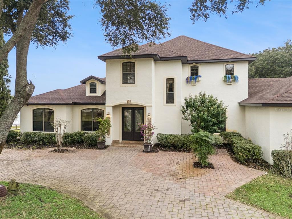 A two-story stucco house with a brick paver driveway and a dark double-door entrance — 19949 S BUCKHILL ROAD, CLERMONT, FL