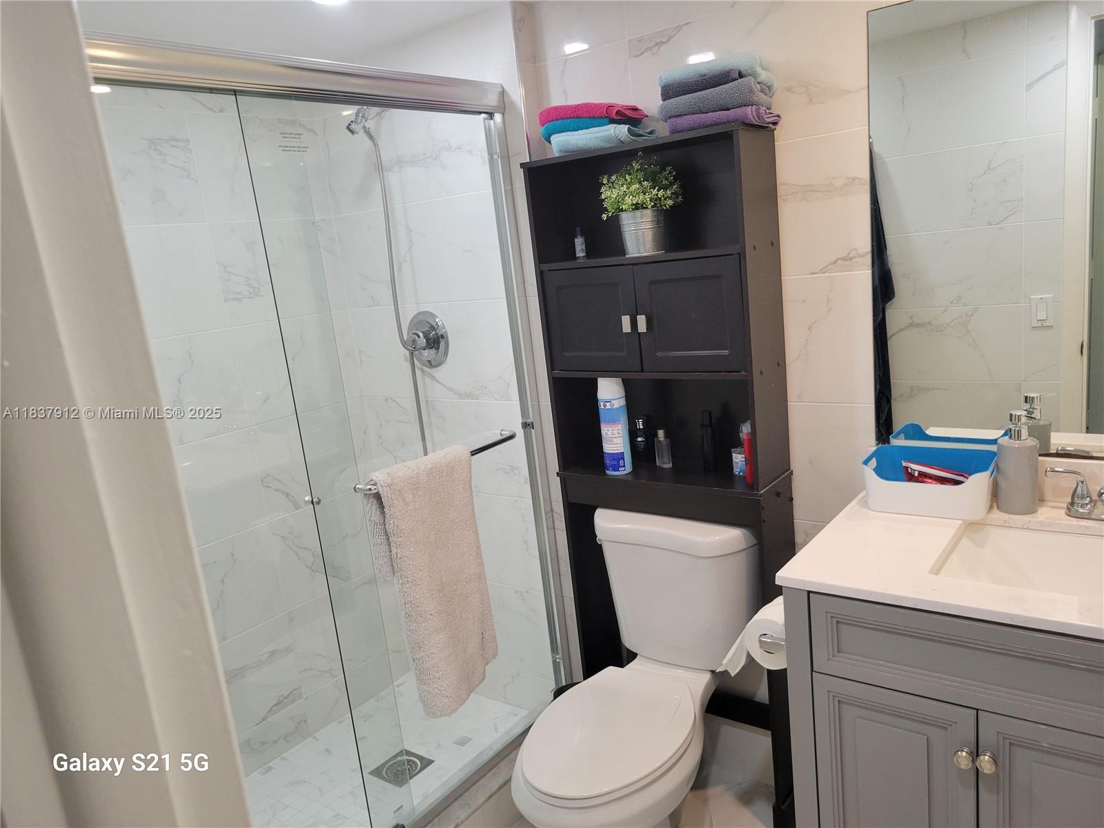 A bathroom features a glass-enclosed shower, a toilet with an over-the-tank shelf, and a vanity — 1849 S Ocean Dr # 1407, Hallandale Beach FL 33009, HALLANDALE BEACH, FL