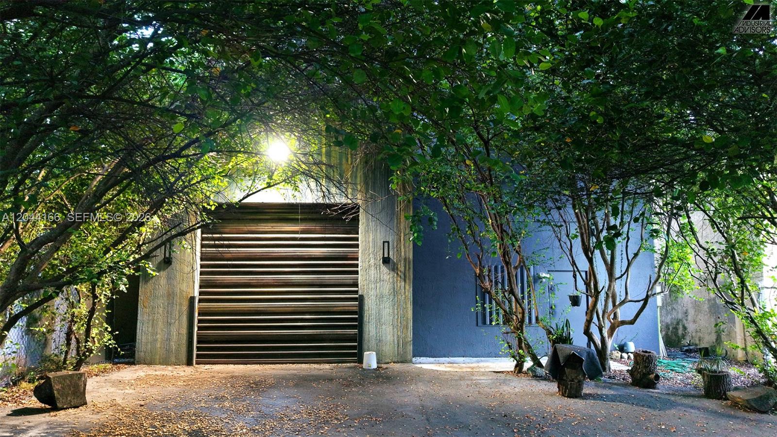 A gray industrial building with a large metal roll-up door sits behind leafy trees — 2310 W 79th St, Hialeah FL 33016, HIALEAH, FL