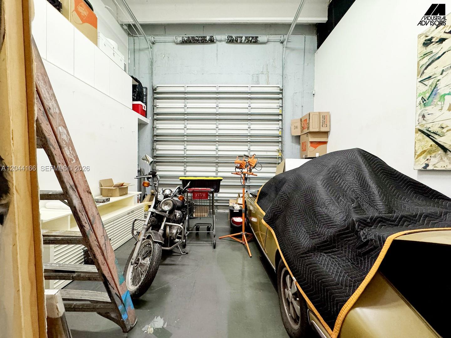 A garage space features a motorcycle, a covered vehicle, and a large roll-up door — 2310 W 79th St, Hialeah FL 33016, HIALEAH, FL