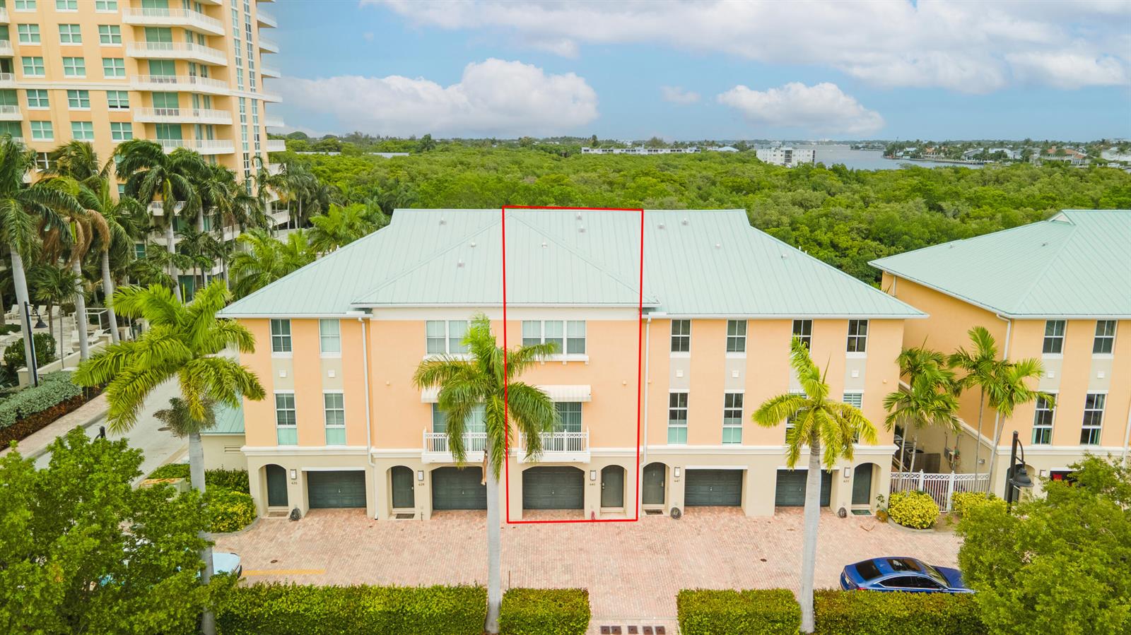 An exterior view of a three-story peach-colored townhouse with a metal roof and palm trees — 643 Casa Loma Boulevard, Boynton Beach FL 33435, BOYNTON BEACH, FL