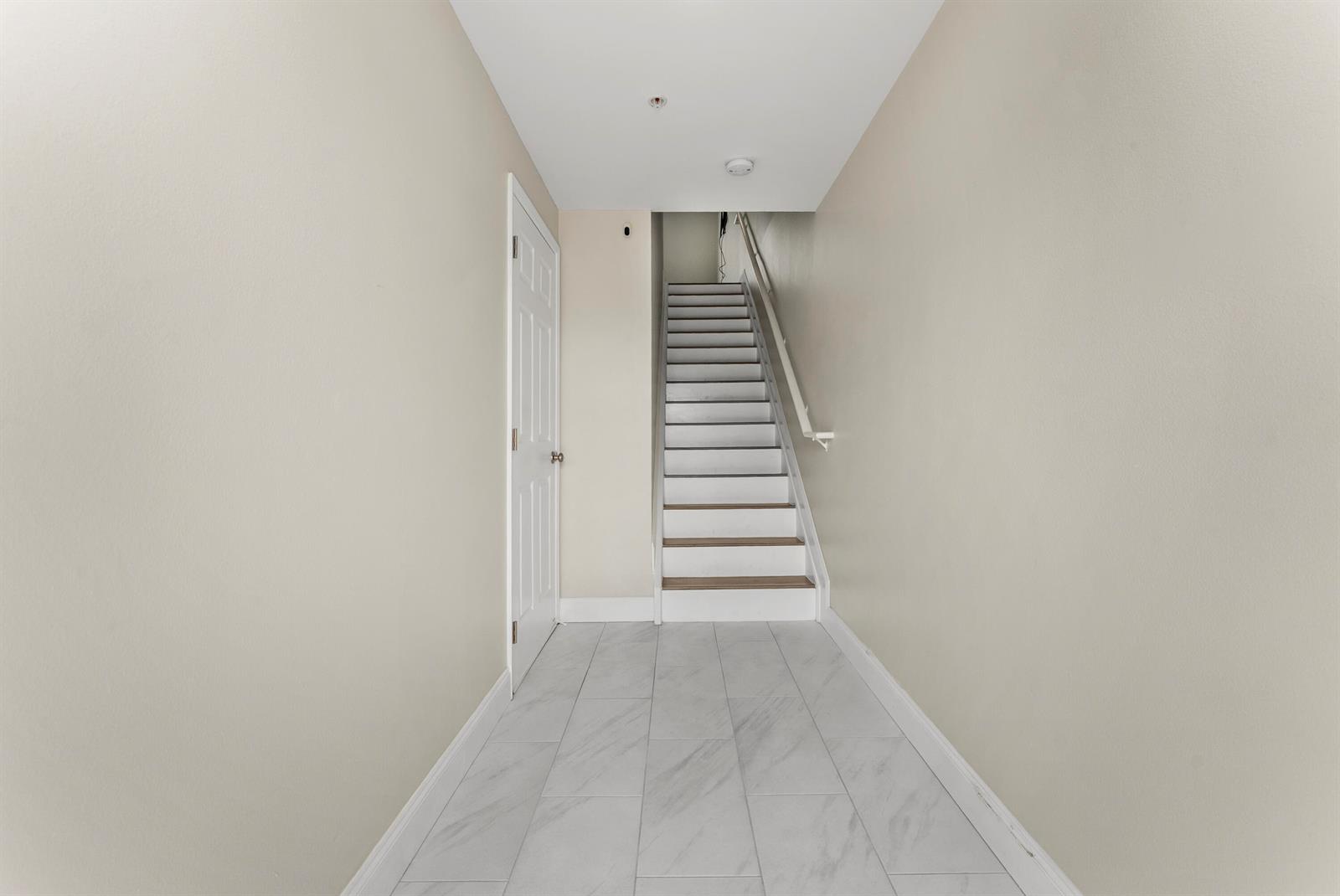 A hallway with light-colored walls and tile flooring leads to a staircase with white risers — 643 Casa Loma Boulevard, Boynton Beach FL 33435, BOYNTON BEACH, FL