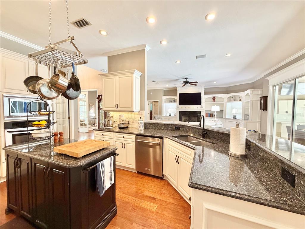 A kitchen with a dark island, granite countertops, white cabinets, and an open living area — 8613 SW 39TH LANE, GAINESVILLE, FL