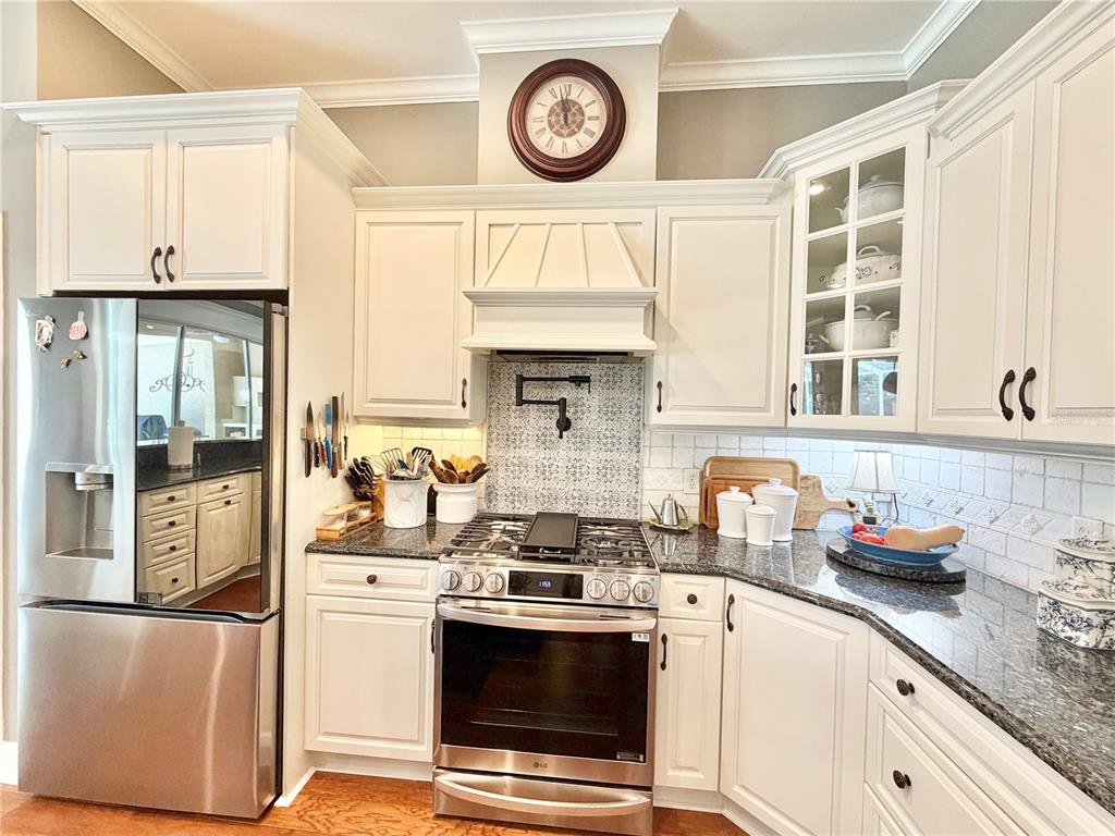 A kitchen features white cabinetry, stainless steel appliances, a patterned backsplash, and a wall clock — 8613 SW 39TH LANE, GAINESVILLE, FL