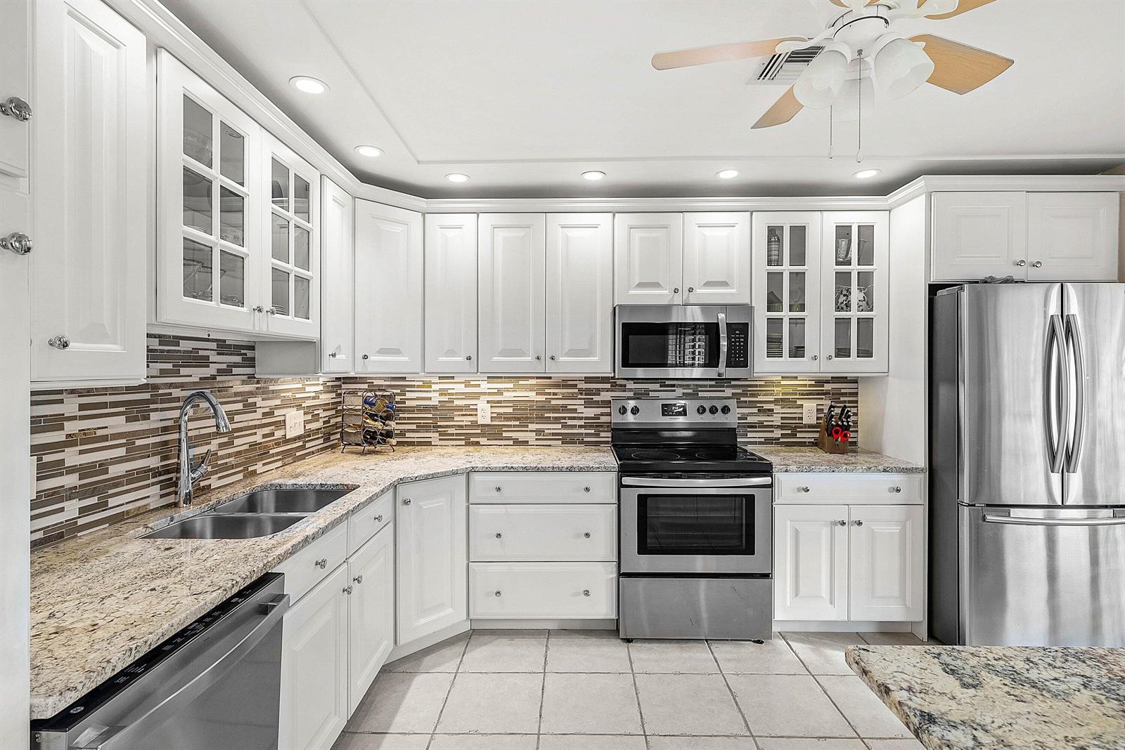 A kitchen features white cabinets, granite countertops, stainless steel appliances, and a tiled backsplash — 11272 Quail Covey Road, Boynton Beach FL 33436, BOYNTON BEACH, FL