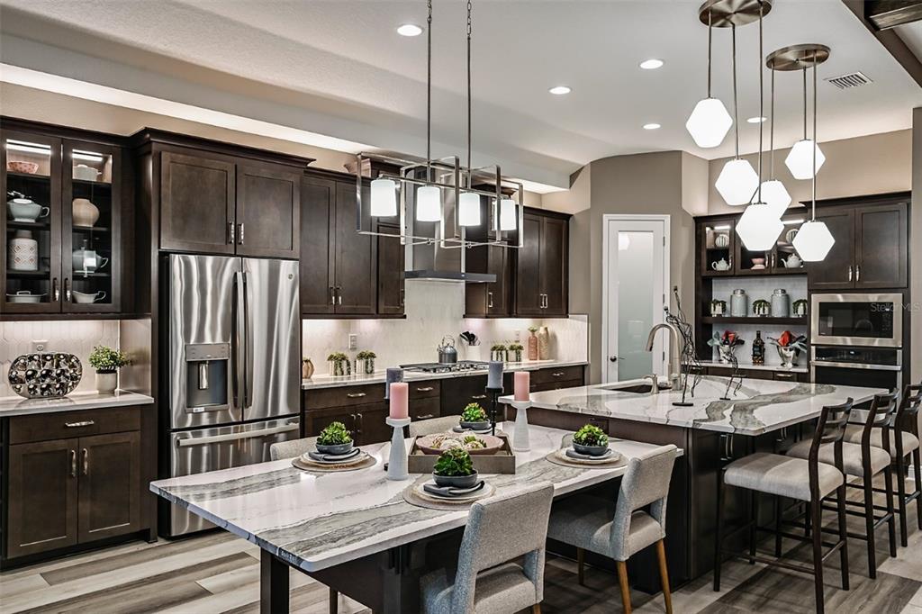 A modern kitchen features dark wood cabinets, marble countertops, stainless steel appliances, and pendant lighting — 5373 WOLF CREEK DRIVE, APOLLO BEACH, FL