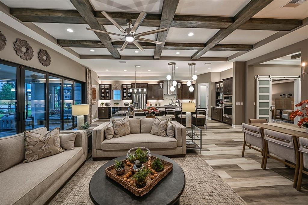 An open-concept living room and kitchen feature wood-beamed ceilings, neutral furniture, and wood-look flooring — 5373 WOLF CREEK DRIVE, APOLLO BEACH, FL