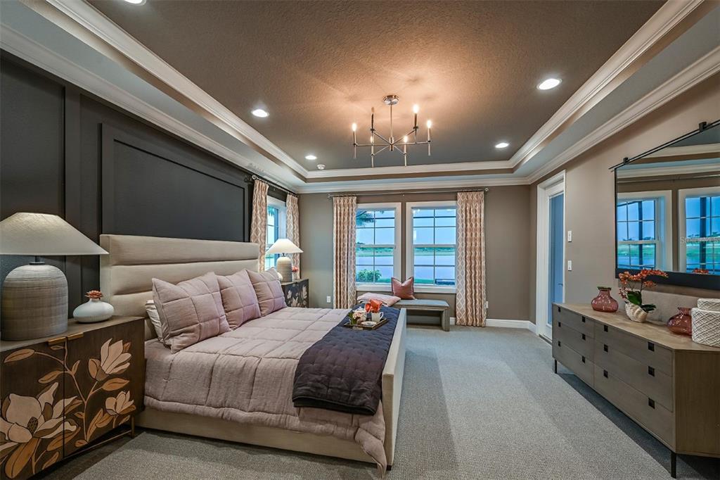 A bedroom features a tray ceiling, dark accent wall, upholstered bed, and a view of water — 5373 WOLF CREEK DRIVE, APOLLO BEACH, FL