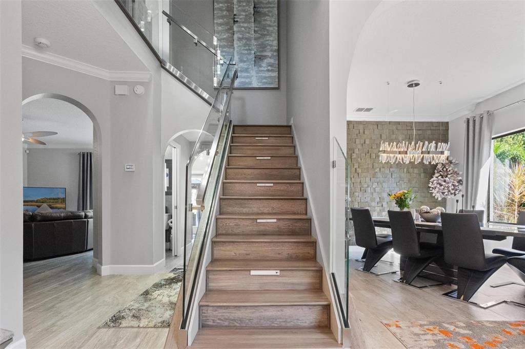 A wooden staircase with glass railings sits between a living room and a dining area — 13228 ROYAL GEORGE AVENUE, ODESSA, FL