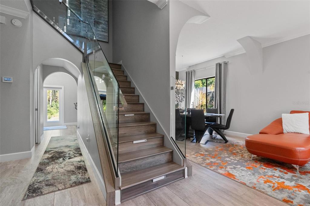 A staircase with glass railings and wood treads sits between a dining area and entryway — 13228 ROYAL GEORGE AVENUE, ODESSA, FL