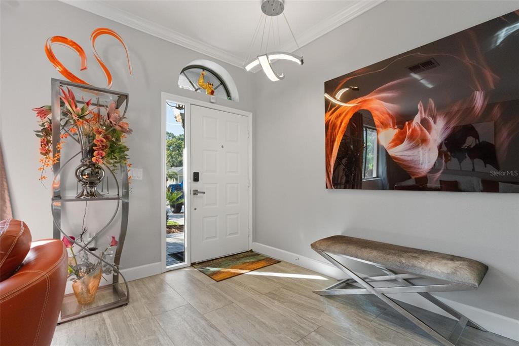 An entryway features light tile floors, a white front door, modern lighting, and decorative wall art — 13228 ROYAL GEORGE AVENUE, ODESSA, FL