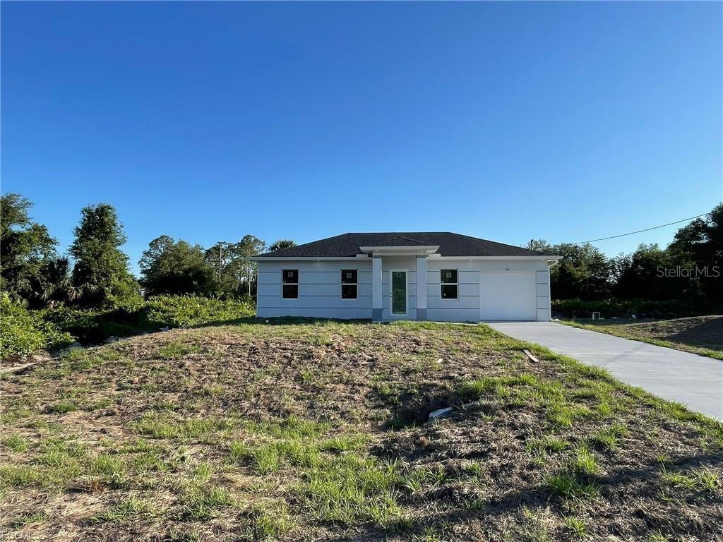 A single-story house with a white exterior, a dark roof, and a concrete driveway — 705 LEDGE STREET, LEHIGH ACRES, FL