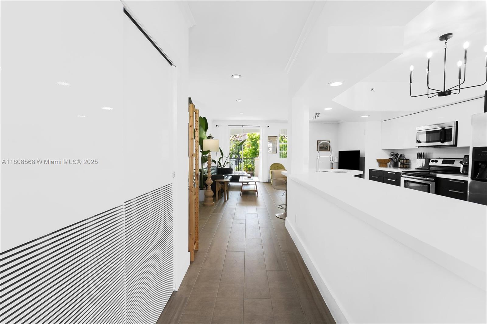 A white kitchen with a breakfast bar overlooks a living area with wood-look flooring — 3245 NE 184th St # 13402, Aventura FL 33160, AVENTURA, FL