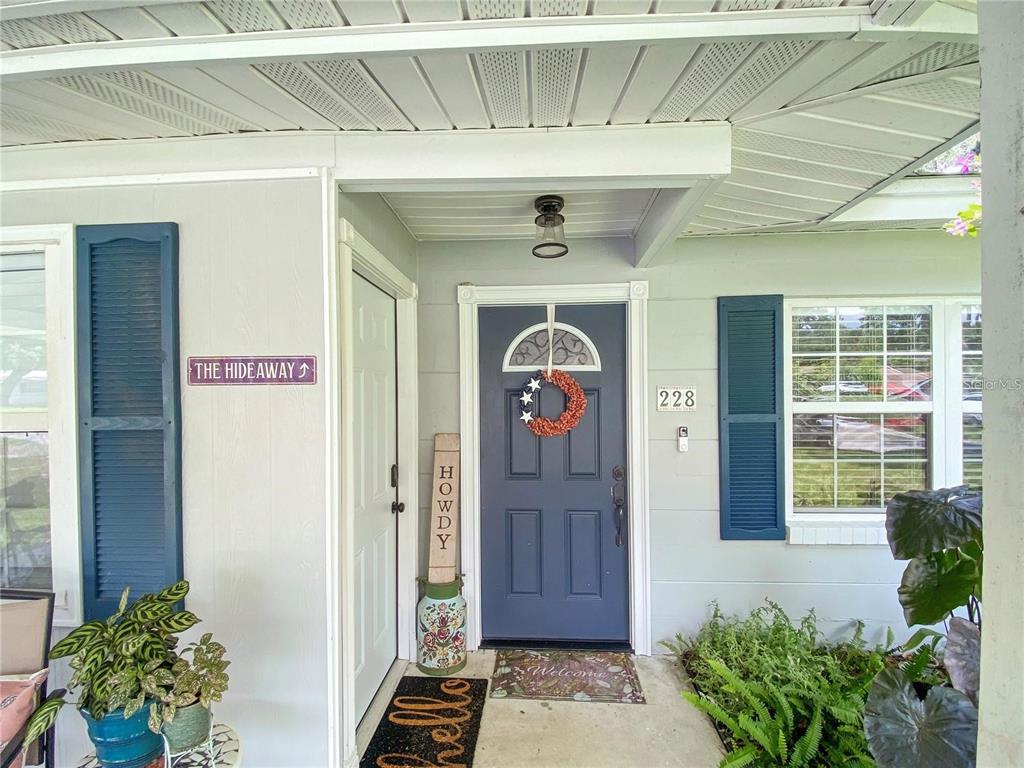 A blue front door with a wreath sits under a covered porch with shutters — 228 SE OAK HILL STREET, LAKE CITY, FL