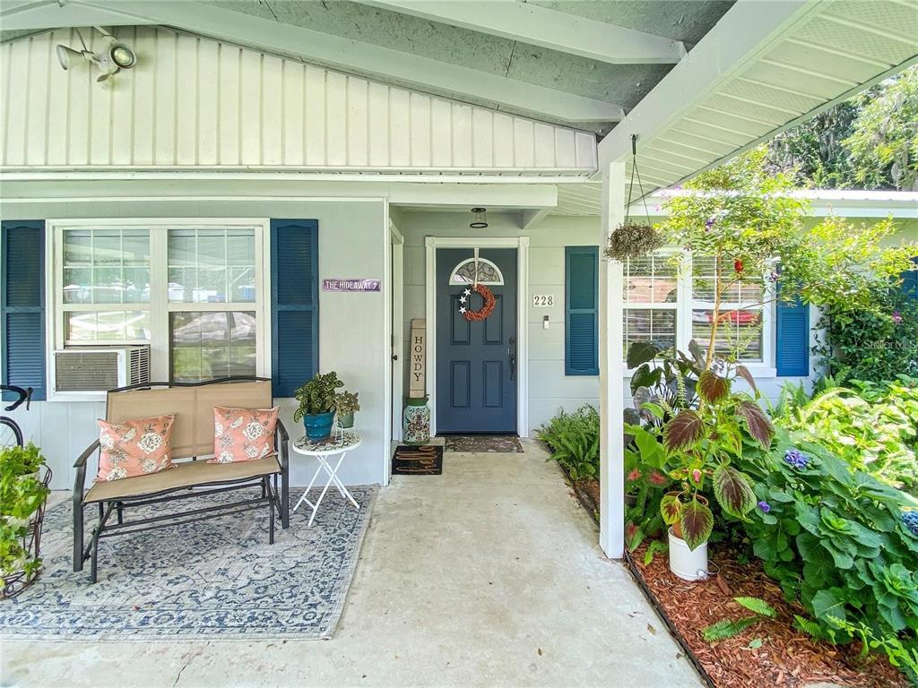 A covered front porch features a bench, a blue front door, and lush potted plants — 228 SE OAK HILL STREET, LAKE CITY, FL