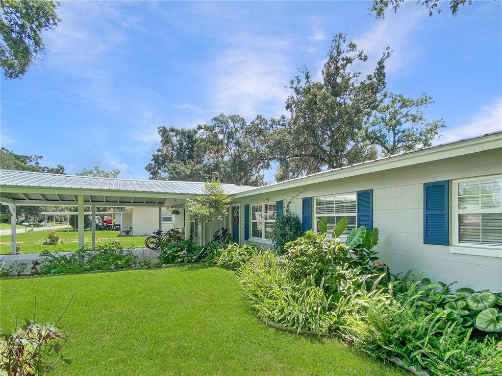 A single-story house with a metal-roofed carport, blue shutters, and a landscaped front yard — 228 SE OAK HILL STREET, LAKE CITY, FL