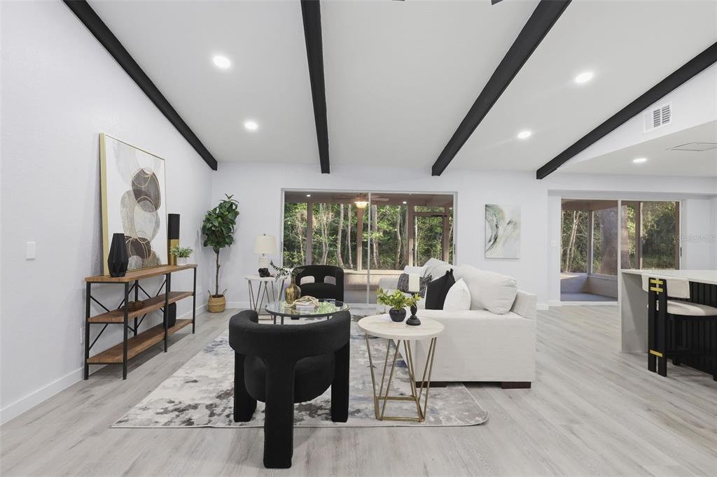 A bright living room features vaulted ceilings with exposed beams, light flooring, and sliding glass doors — 300 E SWEETWATER CREEK DRIVE, LONGWOOD, FL