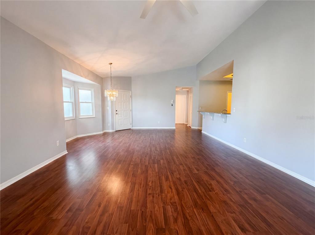 A spacious living room features light gray walls, dark wood-look flooring, and a crystal chandelier — 2320 MARKSMEN COURT UNIT N/A, SUN CITY CENTER, FL