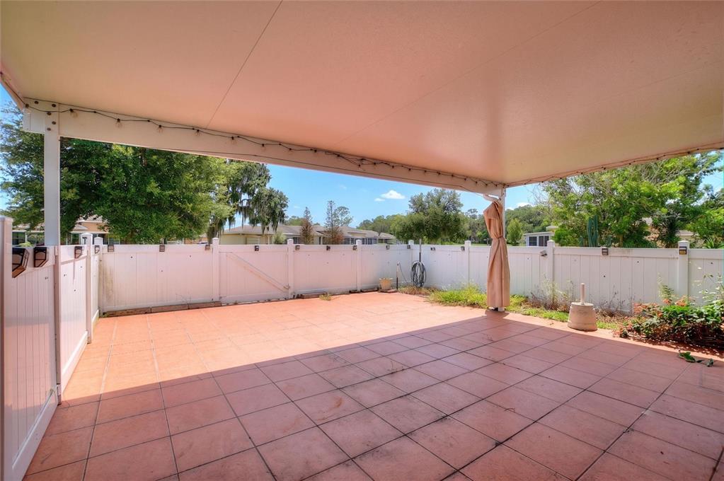 A covered patio with terracotta-colored tile flooring enclosed by a white vinyl privacy fence — 2637 CLUB CIRCLE, LAKE WALES, FL