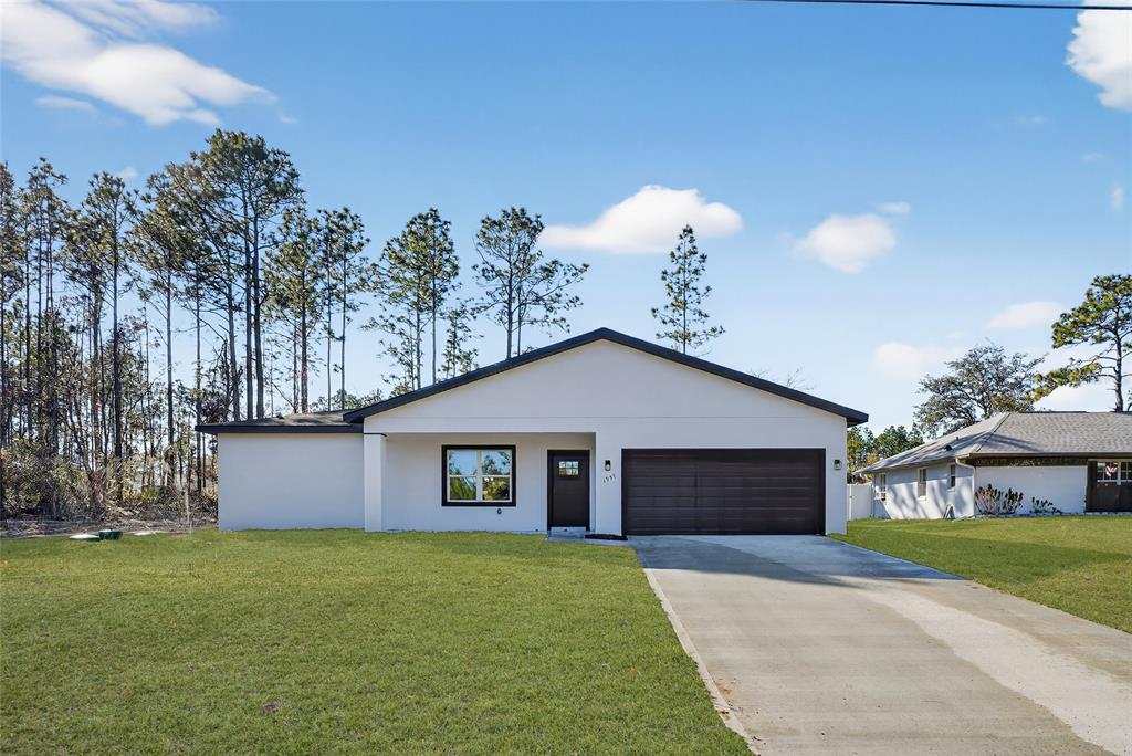 A single-story white house with a dark garage door and a concrete driveway — 1957 W OLIVER DRIVE, CITRUS SPRINGS, FL