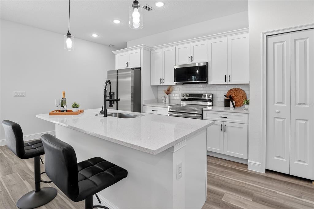 A modern kitchen features white cabinets, a quartz-topped island with bar stools, and stainless appliances — 1957 W OLIVER DRIVE, CITRUS SPRINGS, FL