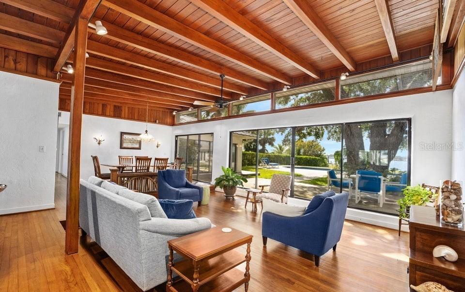 A living and dining area with wood-beamed ceilings, hardwood floors, and large sliding glass doors — 1596 JOHN ANDERSON DRIVE, ORMOND BEACH, FL