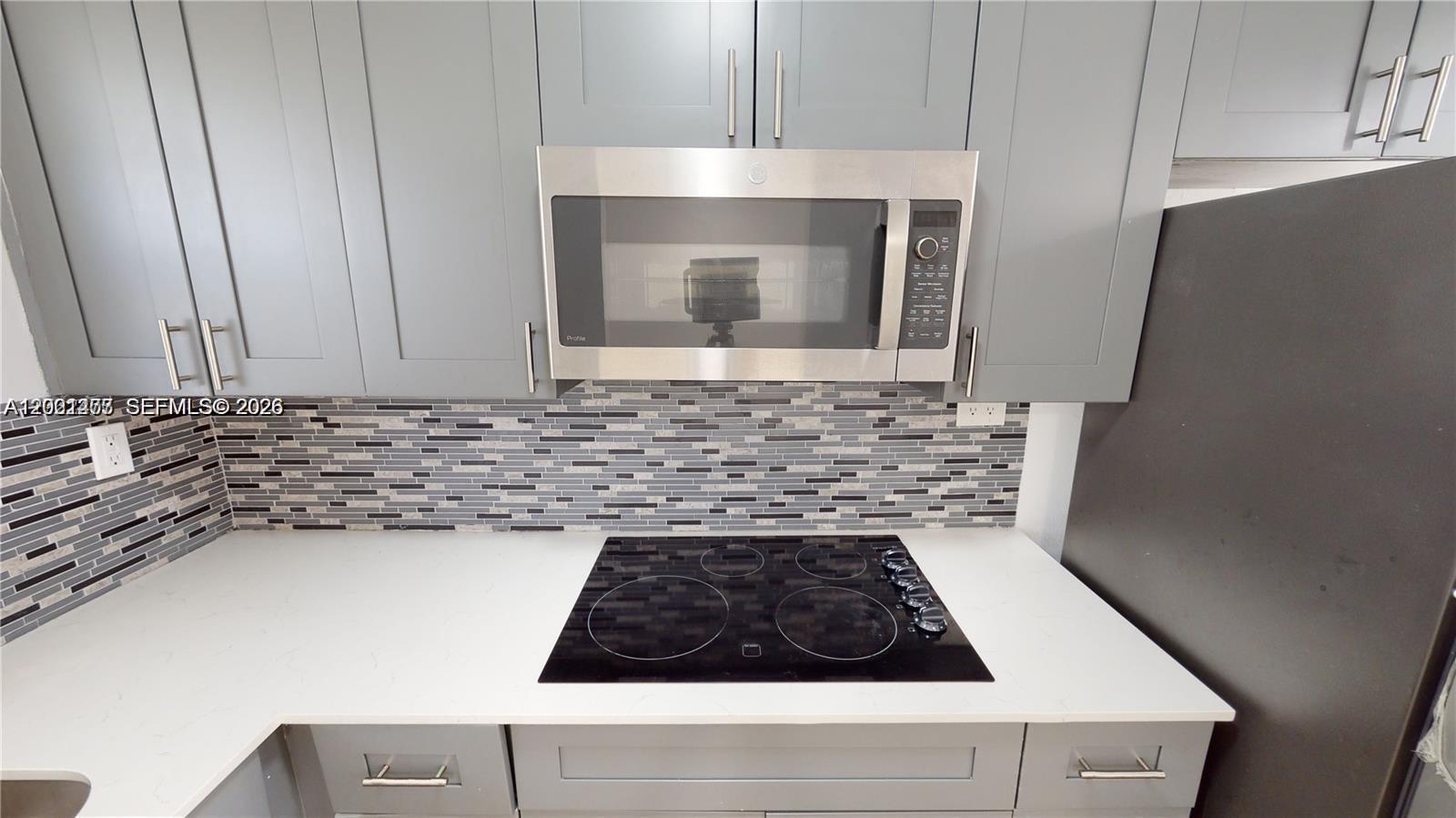 A kitchen features gray cabinets, a stainless steel microwave, a glass cooktop, and tiled backsplash — 453 SW 2nd St # 301C, Miami FL 33130, MIAMI, FL