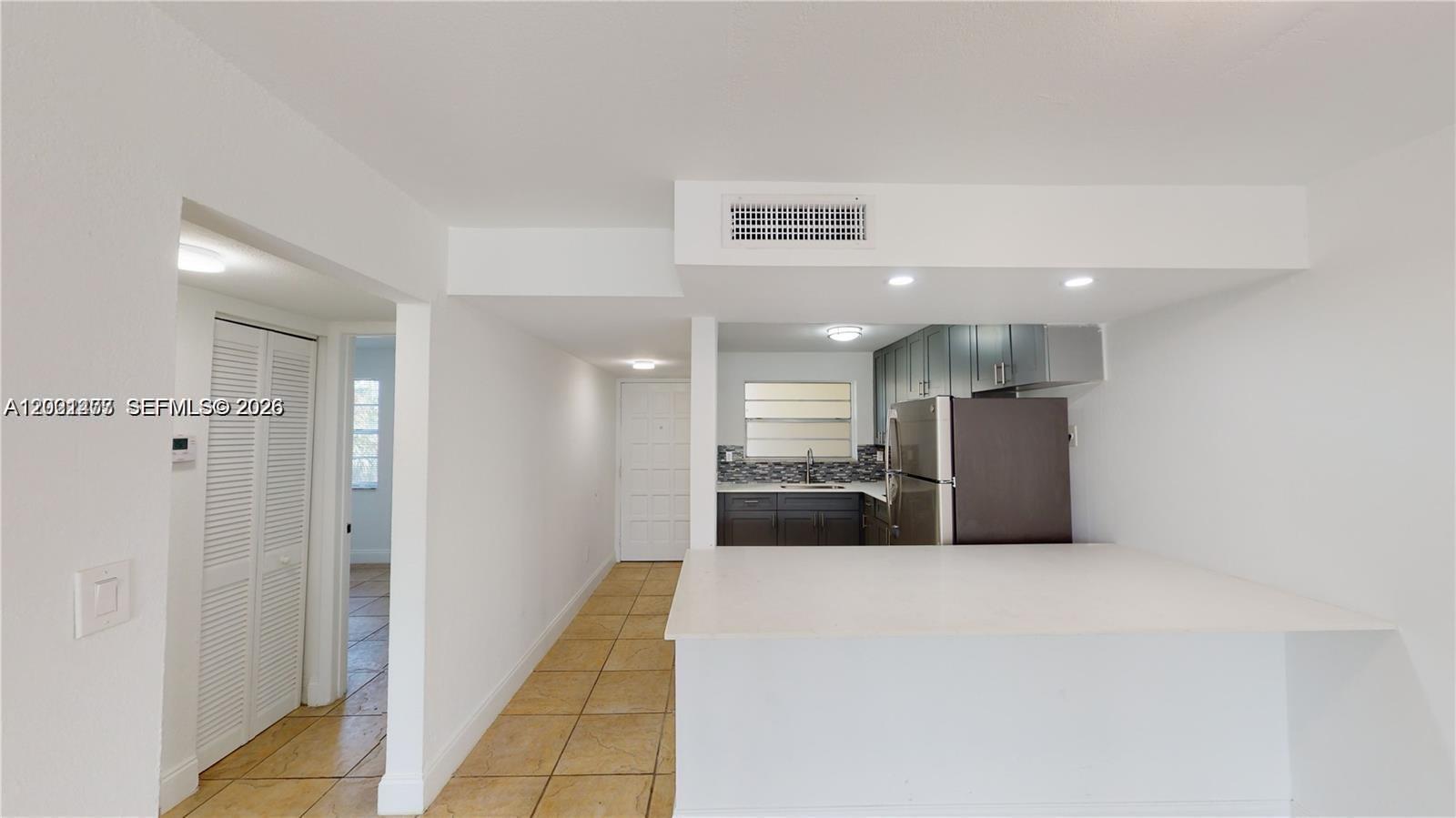 A kitchen with dark cabinets and a white breakfast bar overlooks a tiled hallway — 453 SW 2nd St # 301C, Miami FL 33130, MIAMI, FL