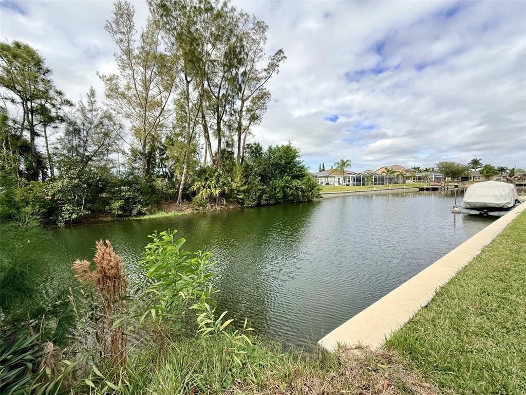 A canal view features a grassy bank, a concrete seawall, and a covered boat — 1414 SW 1ST PLACE, CAPE CORAL, FL